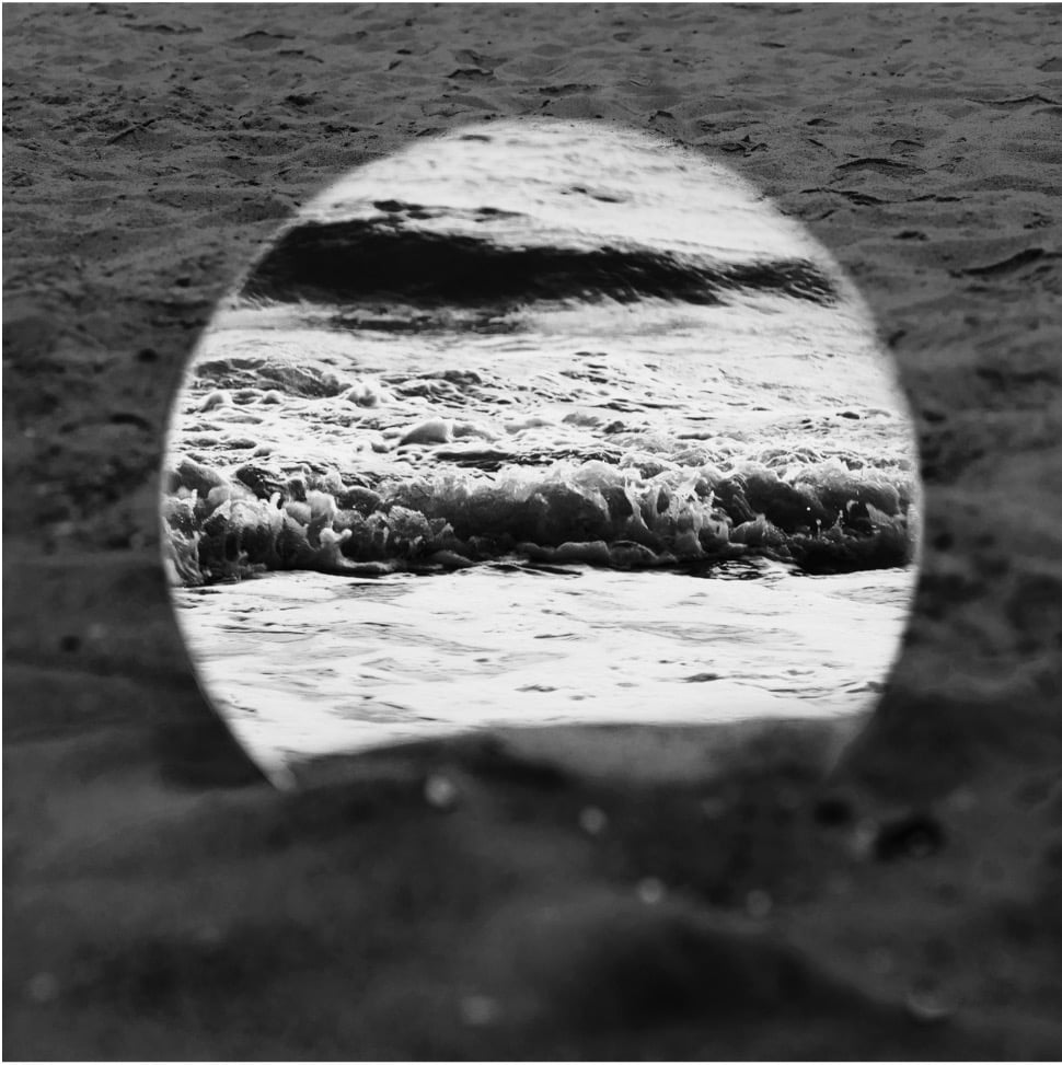Ocean waves framed by an oval opening in dark sand, illustrating focus